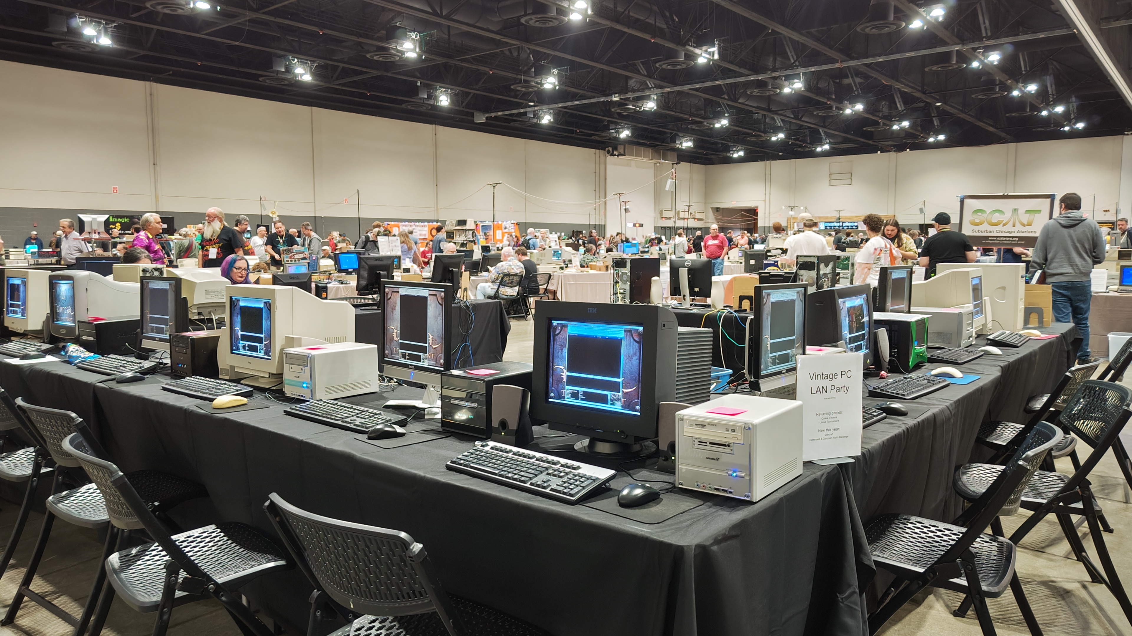 A wide shot of the vintage pc lan party af midwest. The tables are rectangular and positioned to form a square layout. There are 10 pcs 8 chairs visible for people to use to play early 21st century PC games with each other on the local lan.