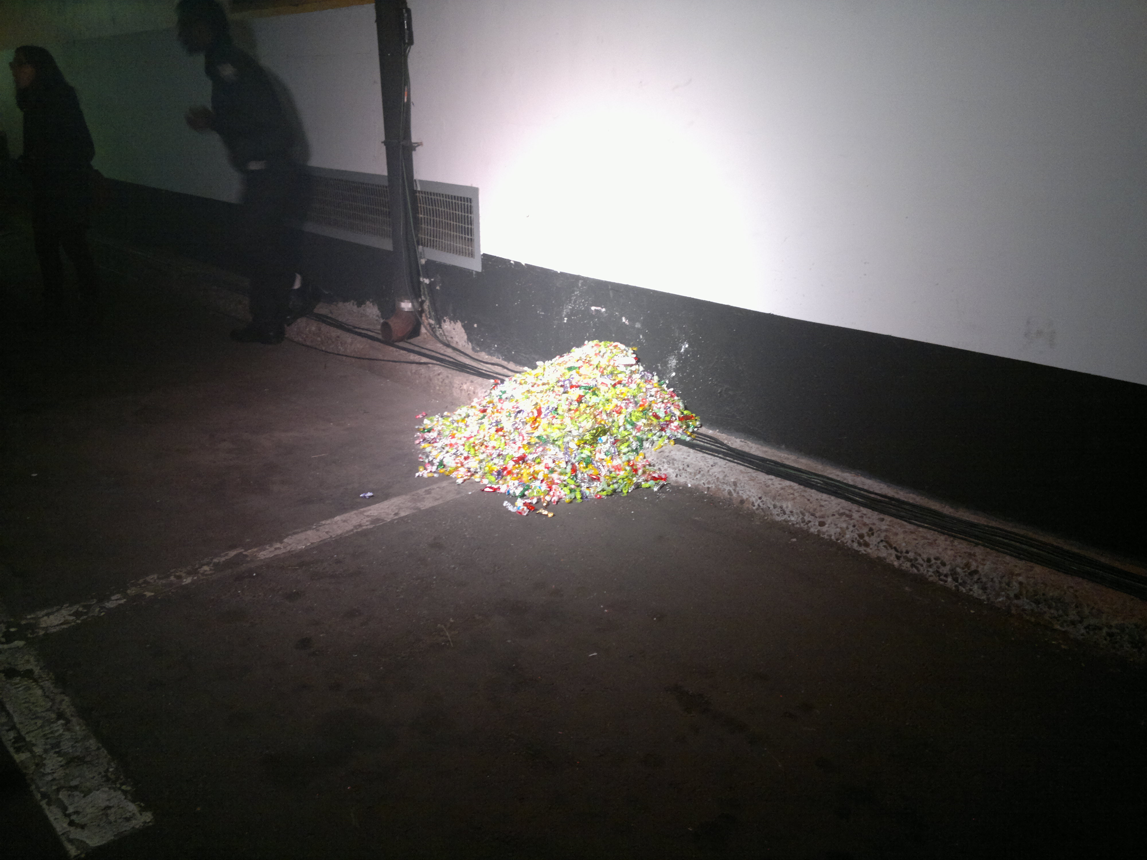 a pile of art, it looks like old candy wrappers, in the parking garage under toronto city hall, lit with a flash in a dark parking garage
