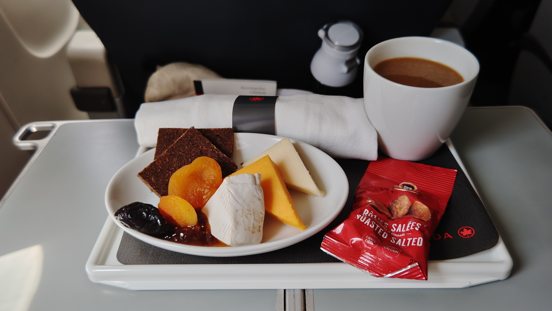 A Rye bread apricot and raspberry jam with brie and cheese with coffee and a package of nuts