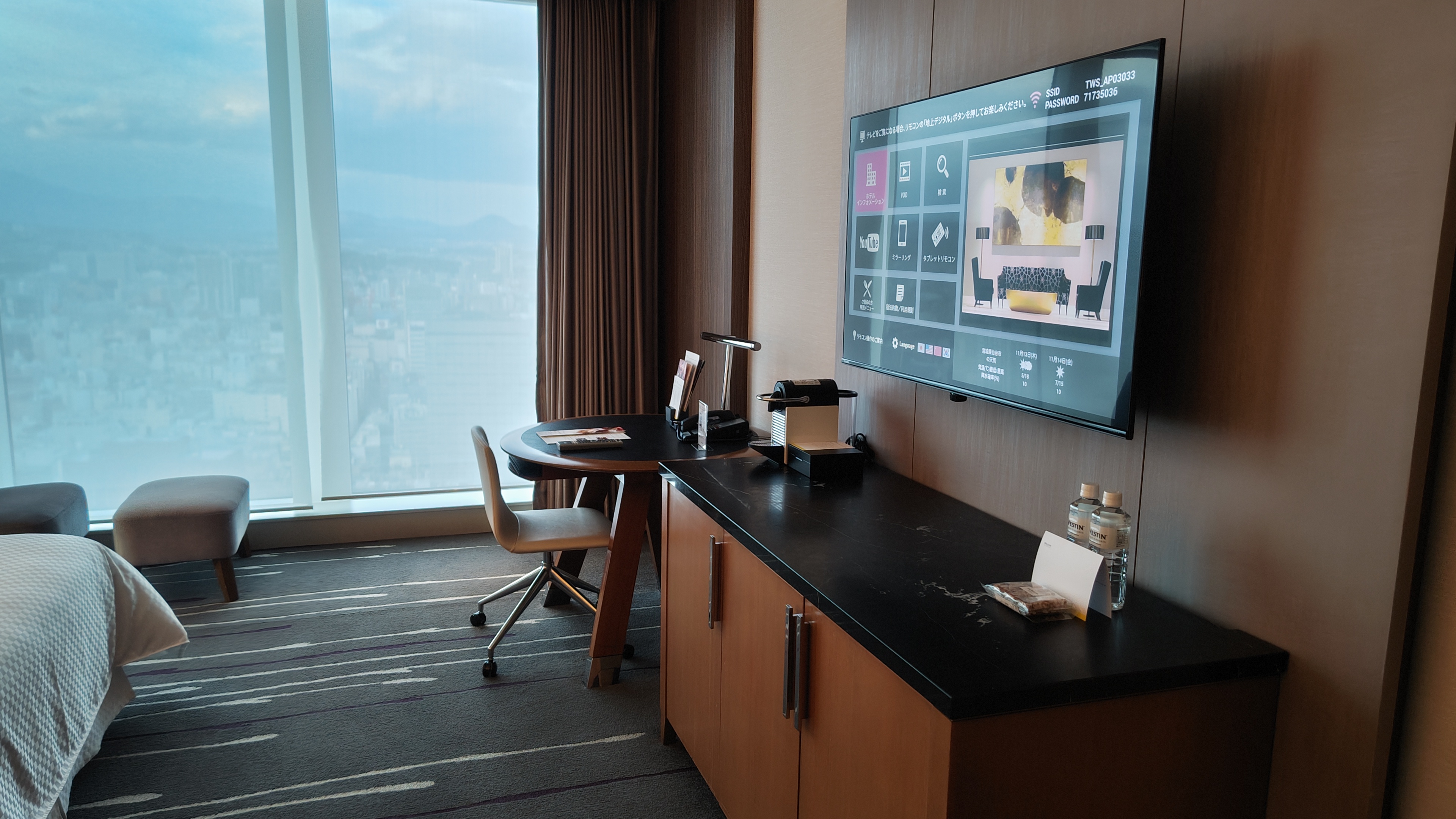 A view of a tv, the cabinet beneath, a table, and view out the window with drapes.