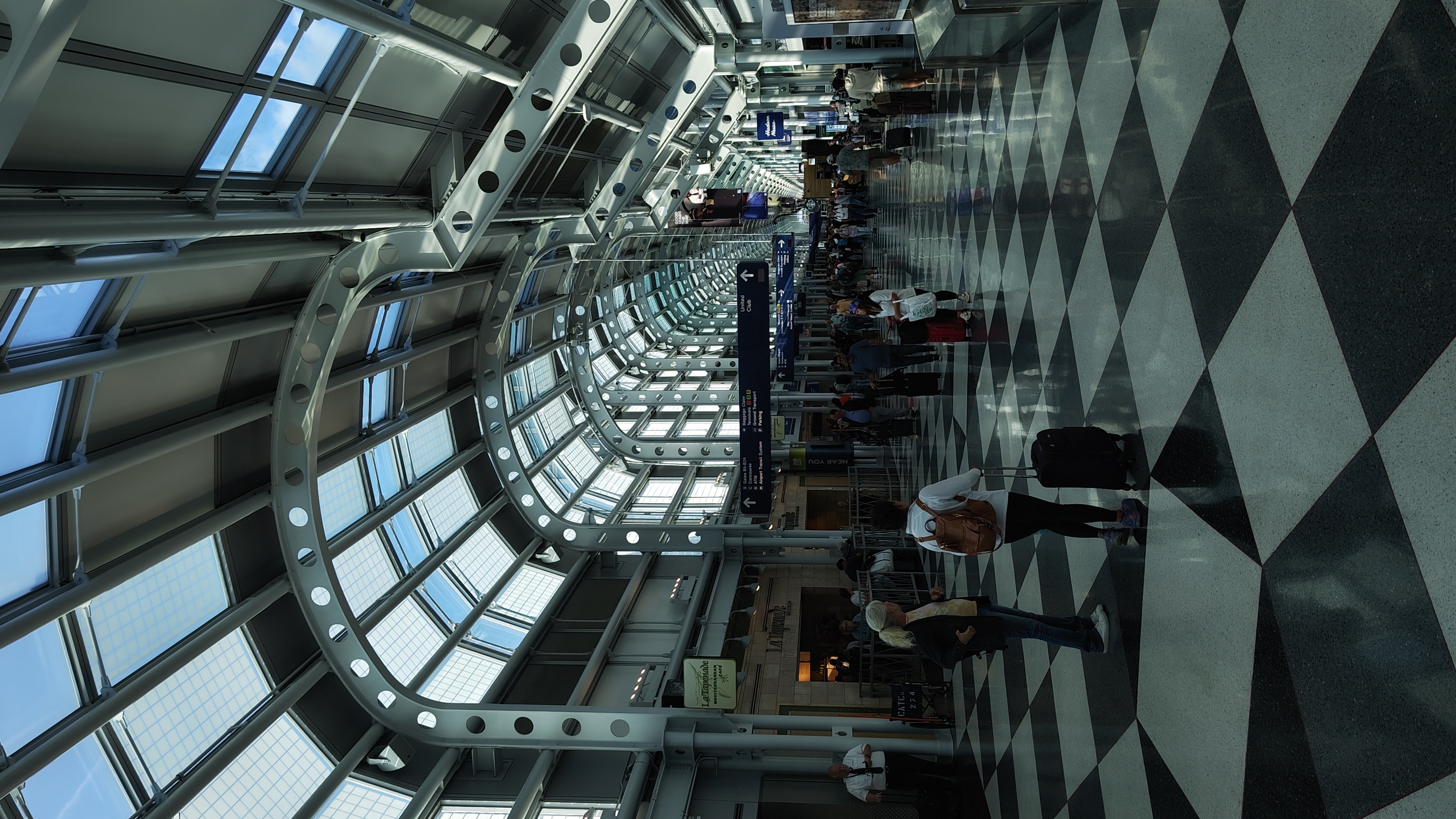 A photo in the late afternoon of O'Hare's passenger terminal interior airside. There are curved roofs with visible beams, and a tiled patterned floor.